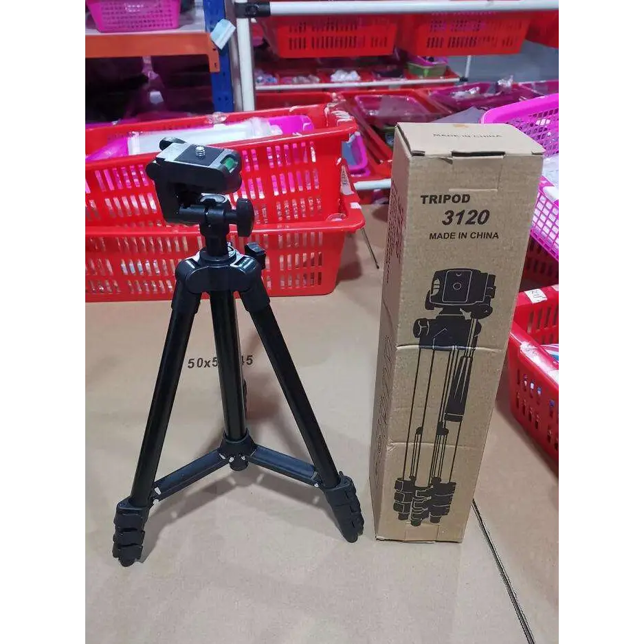 Black portable tripod universal digital camera bracket with adjustable legs standing next to cardboard box labeled tripod 3120 made in china