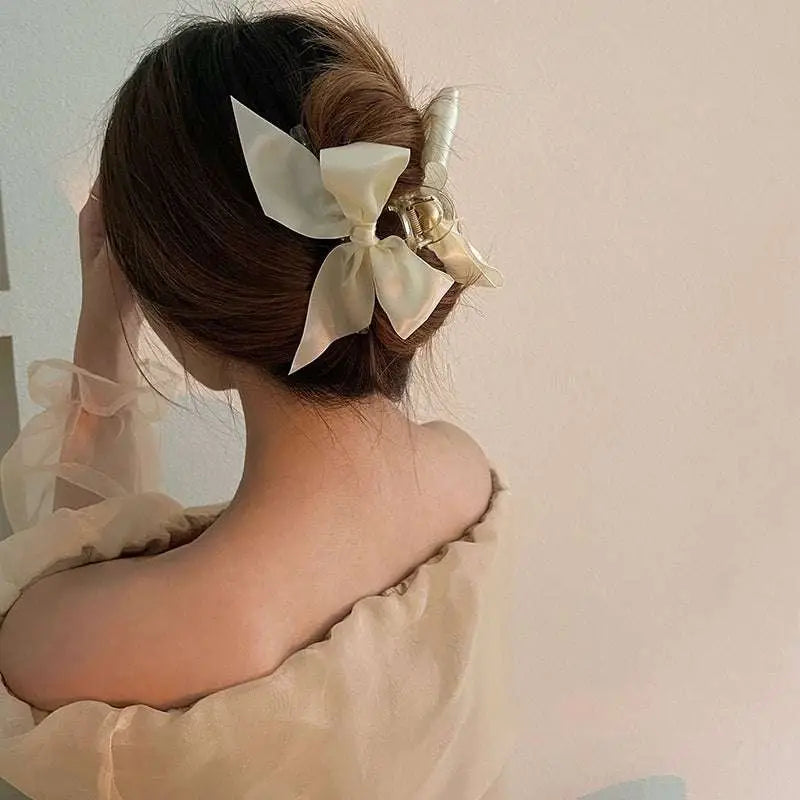 Cream-colored satin female graceful bow grip with a gold-toned metal clasp for elegant hairstyling