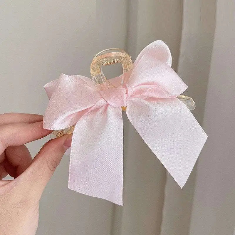 A delicate pink satin female graceful bow grip shark clip with a transparent plastic hair clip base