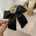Elegant black satin female graceful bow grip shark clip with gold-accented clear claw mechanism for secure hold