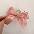 A delicate pink satin female graceful bow grip shark clip with a clear plastic clasp for elegant hairstyling