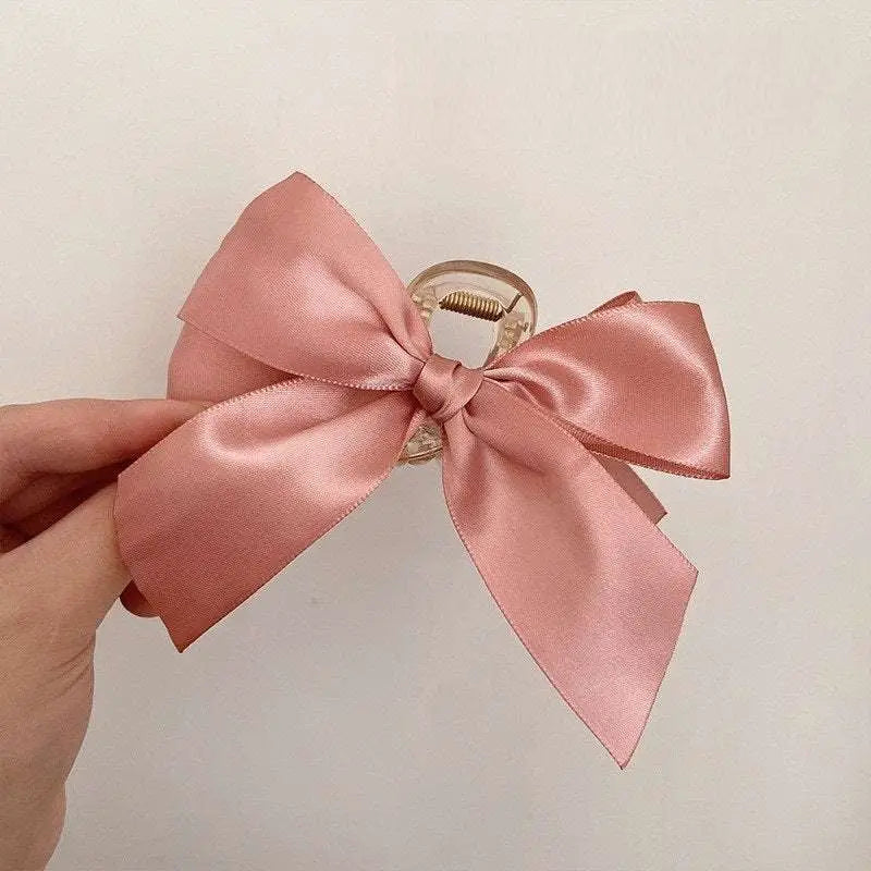 A delicate pink satin female graceful bow grip shark clip with a clear plastic clasp for elegant hairstyling
