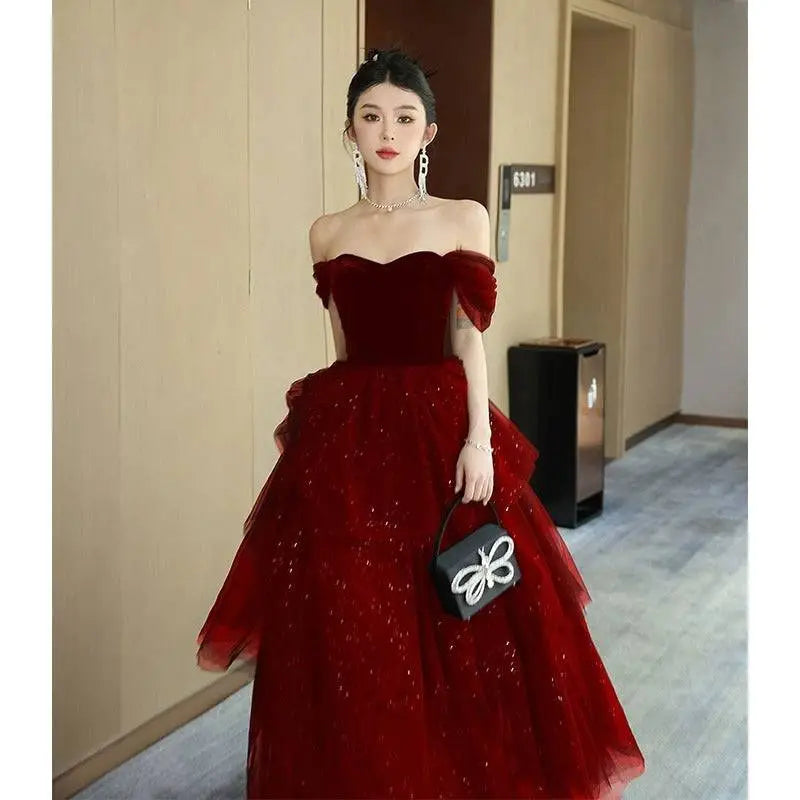 A woman wears a deep red velvet off-the-shoulder gown with tulle light luxury evening detailing and black velvet accents
