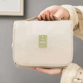 Beige travel toiletry bag with green airplane patch alongside black wall mounted portable women makeup bag displayed