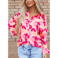 A woman wearing a vibrant pink blooming floral print shirt with long print puff sleeves and coral accents