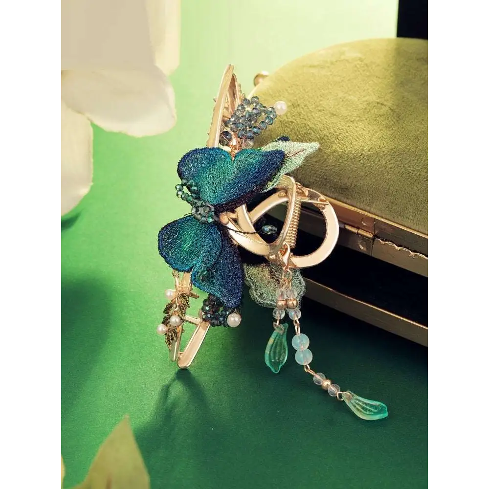 Blue butterfly mori style shark clip with gold-toned metal, teal embroidered wings, beads, pearls, and glass charms