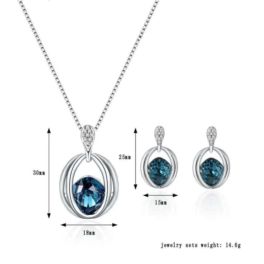 Silver crystal bridal necklace with blue gemstone pendant encased in interlocking rings and diamond accented bail earrings set featuring