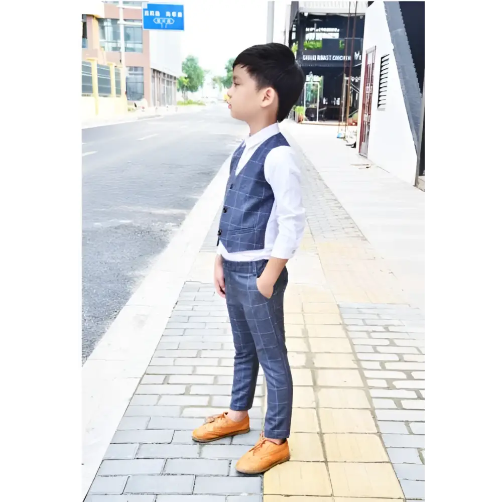 A young boy wearing a blue plaid children’s three-piece fashion suit with a navy comfort vest and trousers