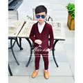 A young boy wearing a maroon velvet children’s three-piece fashion suit with matching trousers and a white shirt