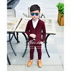 A young boy wearing a maroon velvet children’s three-piece fashion suit with matching trousers and a white shirt