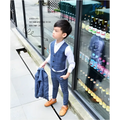 A young boy wearing a blue plaid children’s three-piece fashion comfort suit with matching trousers and orange shoes