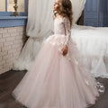 A young girl wears a blush pink lace princess dress flower girl evening dress with long sleeves and embroidered bodice
