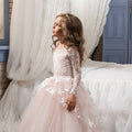 A young girl wearing a blush lace princess dress with intricate white lace sleeves and butterfly appliqués for flower girl evening