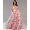 A flowing blush pink mesh evening gown prom with a fitted bodice and voluminous ruffled skirt