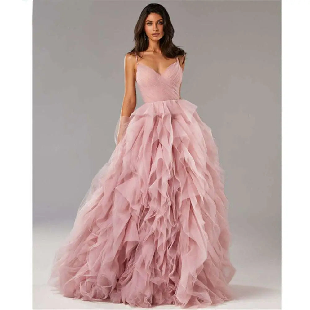A flowing blush pink mesh evening gown prom with a fitted bodice and voluminous ruffled skirt