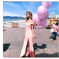 A woman in a blush satin luxury fashion tube dress with a high slit holds light pink balloons on a boardwalk