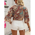 A woman wears a bohemian style printed front tie crop top with vibrant paisley pattern and bell sleeves in red and teal