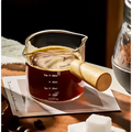 A borosilicate glass espresso measuring cup with wood handle filled with dark espresso and measurement markings