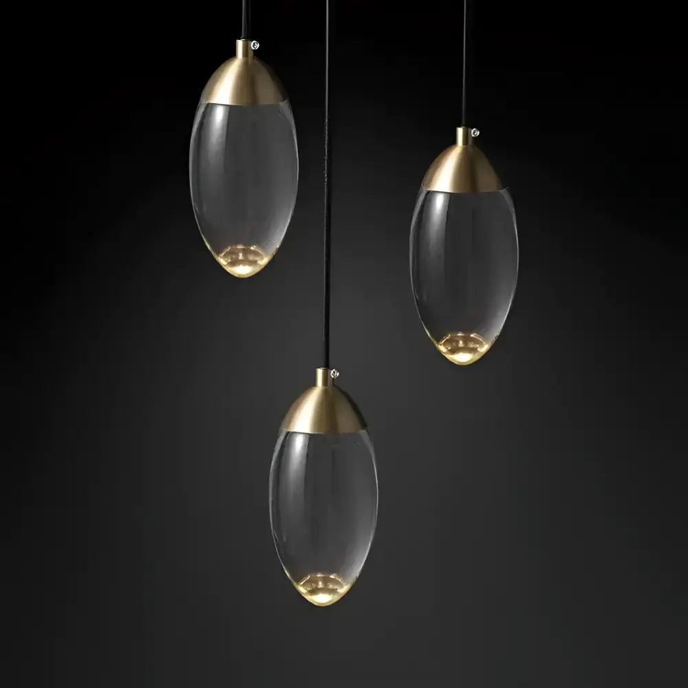 Three elegant brass and glass raindrop pendant lights with clear egg-shaped shades for contemporary elegance