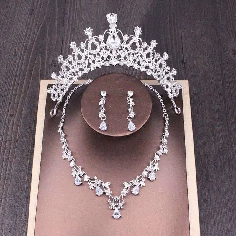 Silver bridal rhinestone crown with intricate floral crystal detailing and central teardrop gemstone in crown necklace set