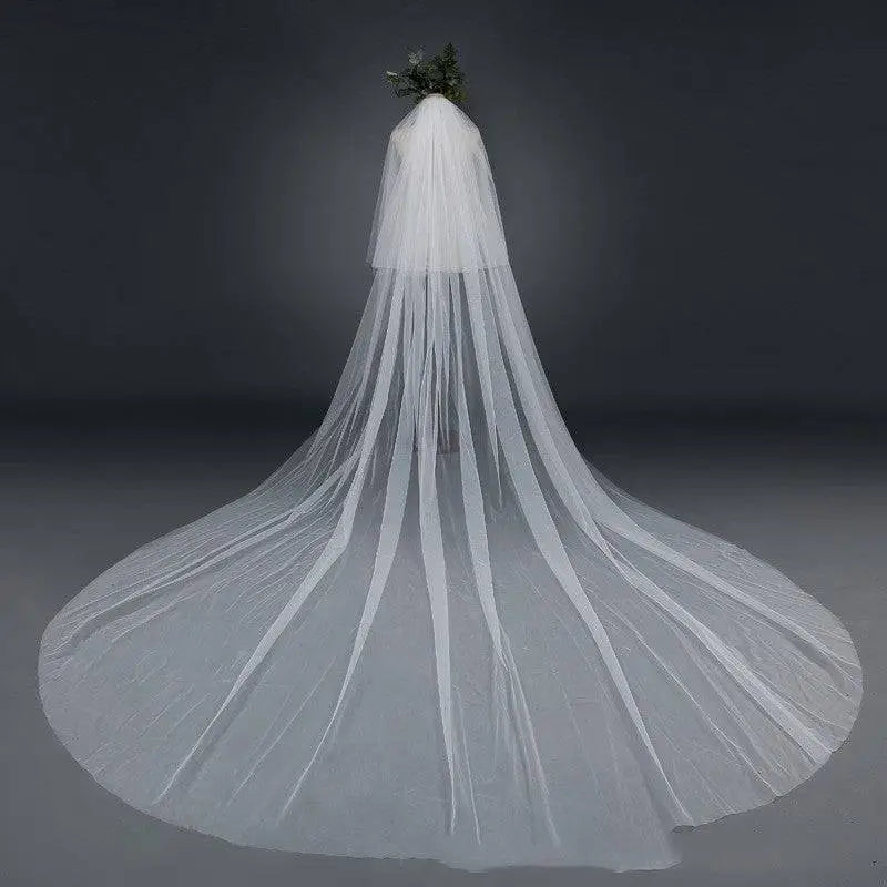 Bridal wedding veil with widened tail in delicate white sheer tulle fabric featuring a hair comb attachment