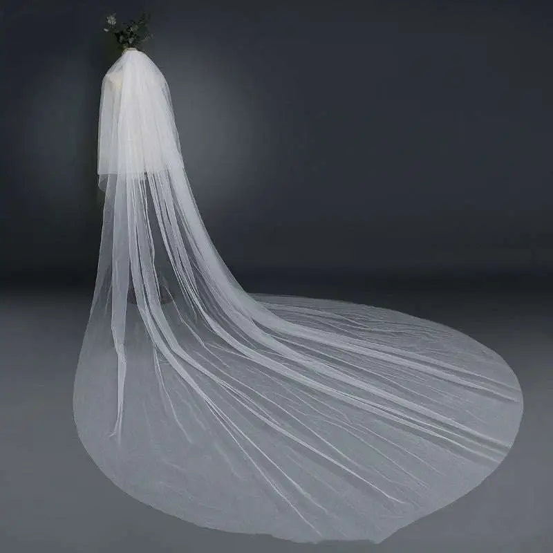 A flowing white bridal wedding veil with a wide tail made of sheer tulle fabric attached to a hair comb