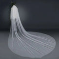A flowing white bridal wedding veil with a wide tail made of sheer tulle fabric attached to a hair comb