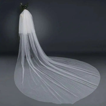 A flowing white bridal wedding veil with a wide tail made of sheer tulle fabric attached to a hair comb