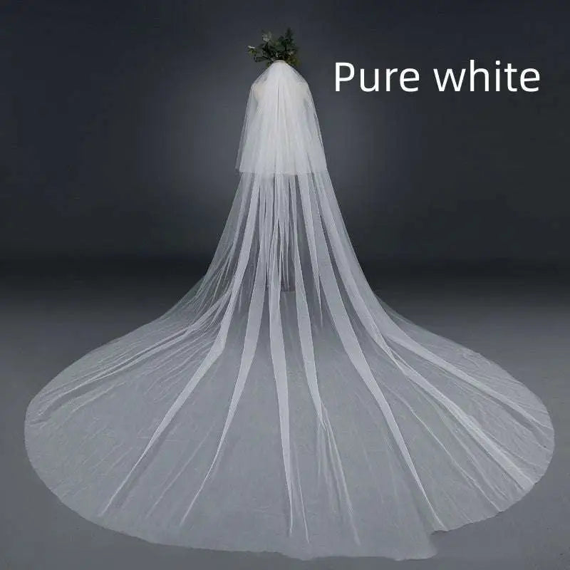 Bridal wedding veil with widened tail made of sheer white tulle fabric gathered at top with attached hair comb