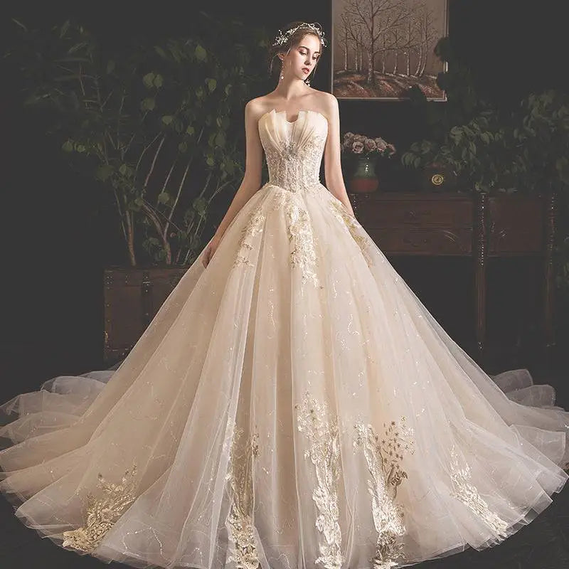 A strapless ivory bride summer tube gown with gold lace appliqués and a mori style trailing skirt of voluminous tulle