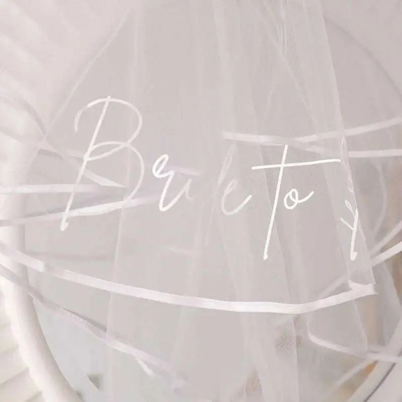 A delicate white tulle double layer veil with bride to be script and bridal comb double for bachelor party bridal use