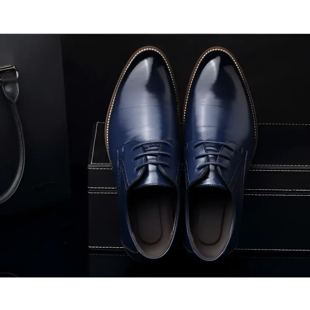 A pair of polished navy blue leather oxford dress business shoes with white stitching and laces