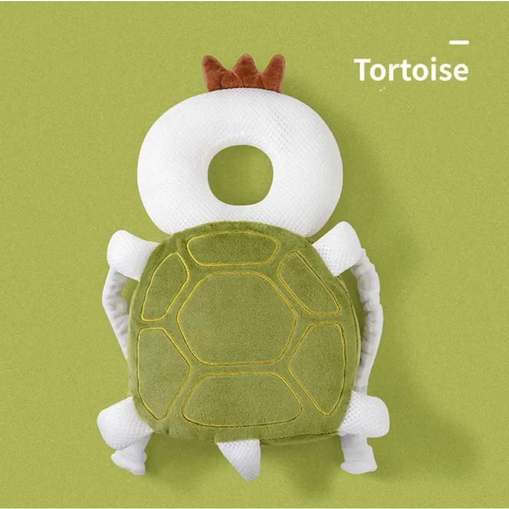 A plush tortoise-shaped toddler head protection pad with a white head, green stitched shell, and bunny ear mesh design
