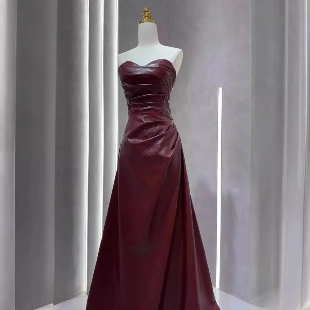 A strapless skirt evening gown in glossy burgundy leather with a fitted bodice and flowing floor-length skirt