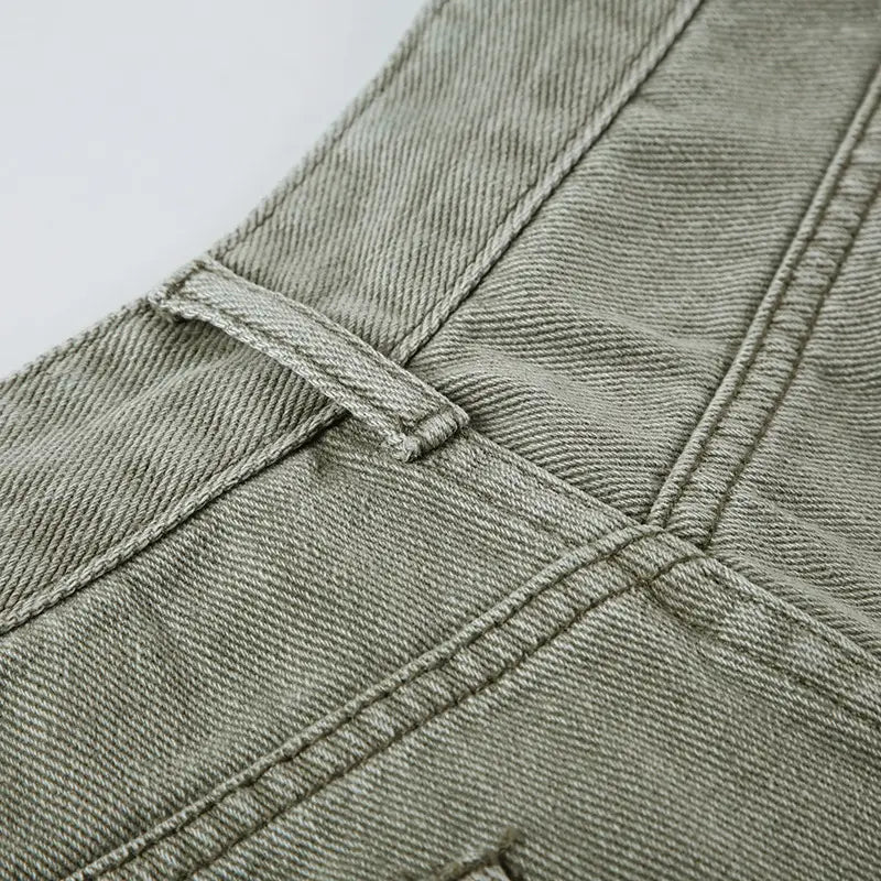 A close-up of light green olive denim jeans double belt adjustable buckle shorts showcasing the textured weave and matching stitching around the waistband.