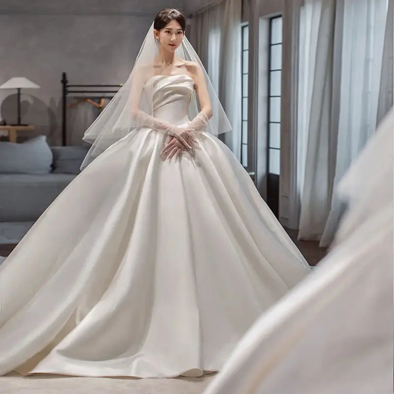 a flowing ivory satin wedding gown with a strapless bodice and expansive ballgown skirt complemented by a matching veil in temperament princess style french satin