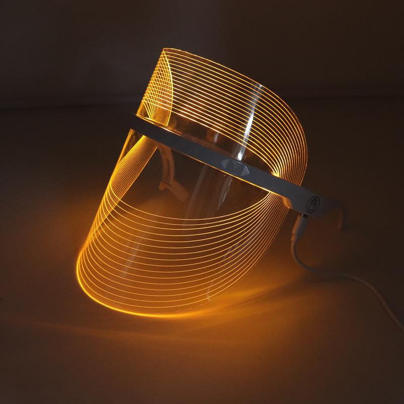 A sleek curved multifunctional facial massager led beauty mask with a transparent visor and glowing amber light strips designed as a lifting tool massager for facial beauty.