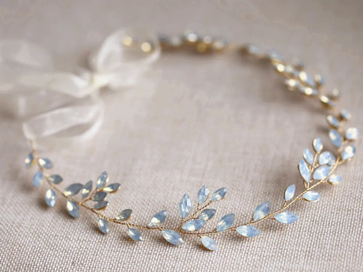 A delicate gold-toned hair band featuring light blue faceted leaf-shaped crystals and a soft white ribbon bow designed as a silver leaf protein rhinestone headdress.