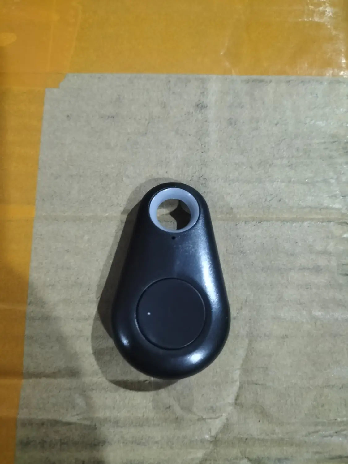 black plastic bluetooth anti lost object finder in a water drop shape with a circular button and keyhole-shaped opening