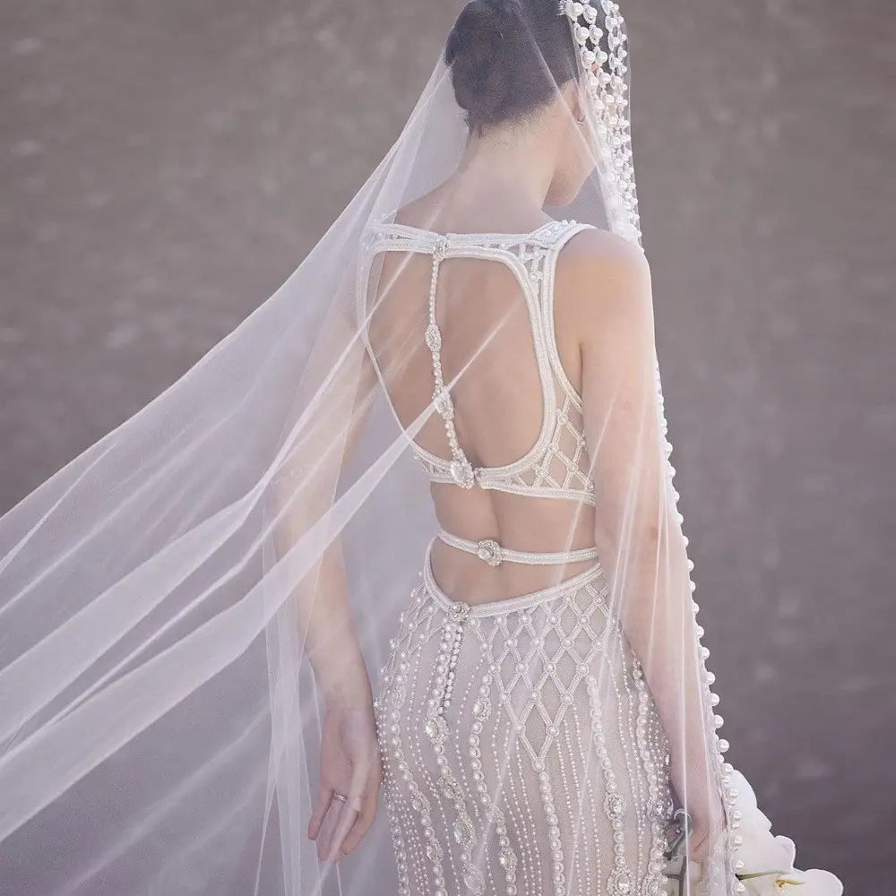 a white beaded wedding gown with lattice back design paired with a trailing yarn wedding bridal veil featuring a broadband hair comb accessory