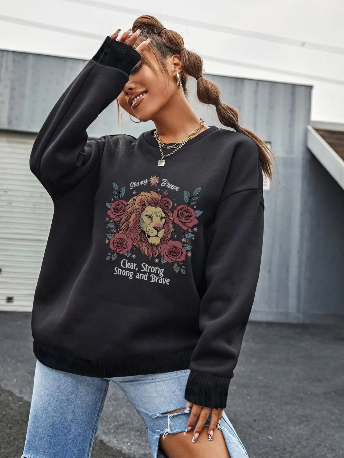 black oversized lion rose regular fit long sleeve sweatshirt featuring a detailed lion face surrounded by roses with the text strong brave above and clear strong strong and brave below