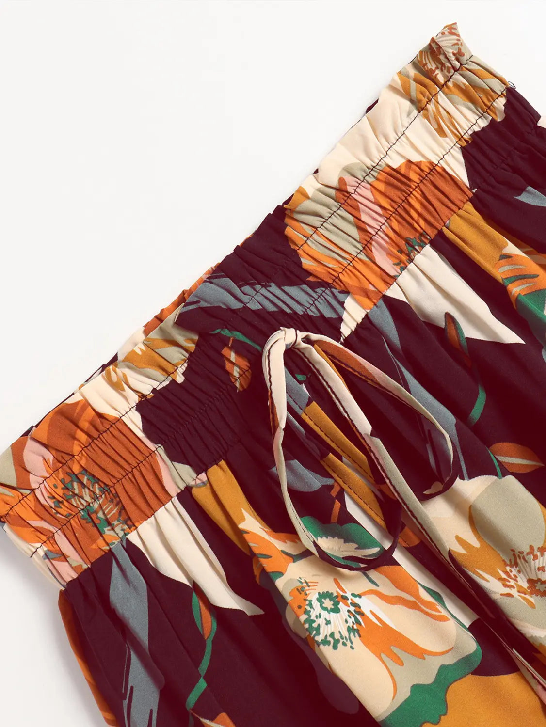 a vibrant high-waisted pair of shorts with a bold tropical pleated floral print elastic waist featuring orange green and cream-colored leaves on a dark maroon background