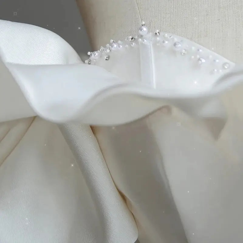 Delicate white satin light wedding dress featuring an off the shoulder design with ruffles adorned by scattered pearl like beads for the wedding dress bride.