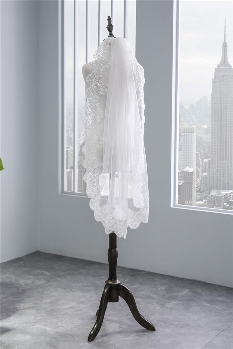 a delicate white ivory short veil soft mesh with sequined lace featuring intricate floral embroidery and a scalloped edge displayed on an elegant mannequin stand