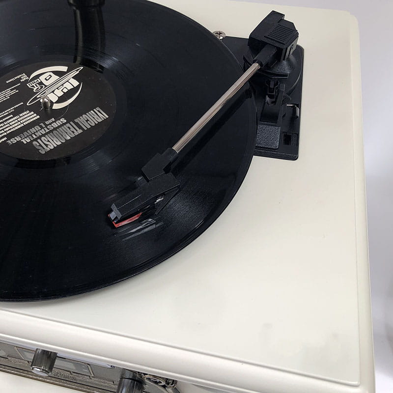 a black vinyl record with a white label featuring the suburban legends logo resting on a cream-colored vintage white gramophone in a classical living room tea setting
