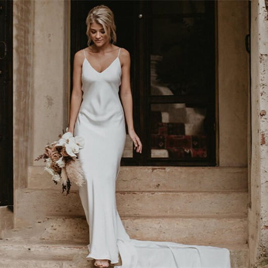 white satin evening gown with a flowing train brigade shot featuring a v-neckline and thin spaghetti straps