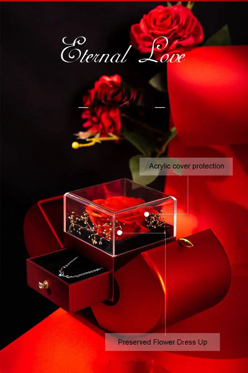 A red apple jewelry box featuring a red preserved rose in a clear acrylic box with gold accents nestled within a matching red velvet-lined drawer.