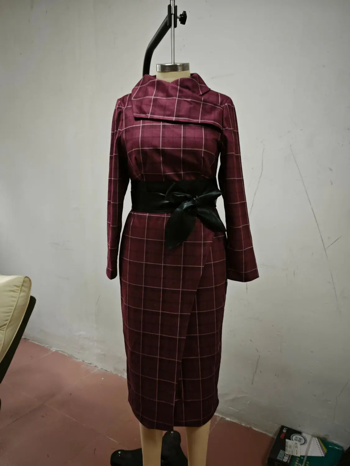 Burgundy high neck wide-waisted belted dress featuring a maroon and white plaid pattern, knee-length design, three-quarter sleeves, and a black satin bow belt at the waist.