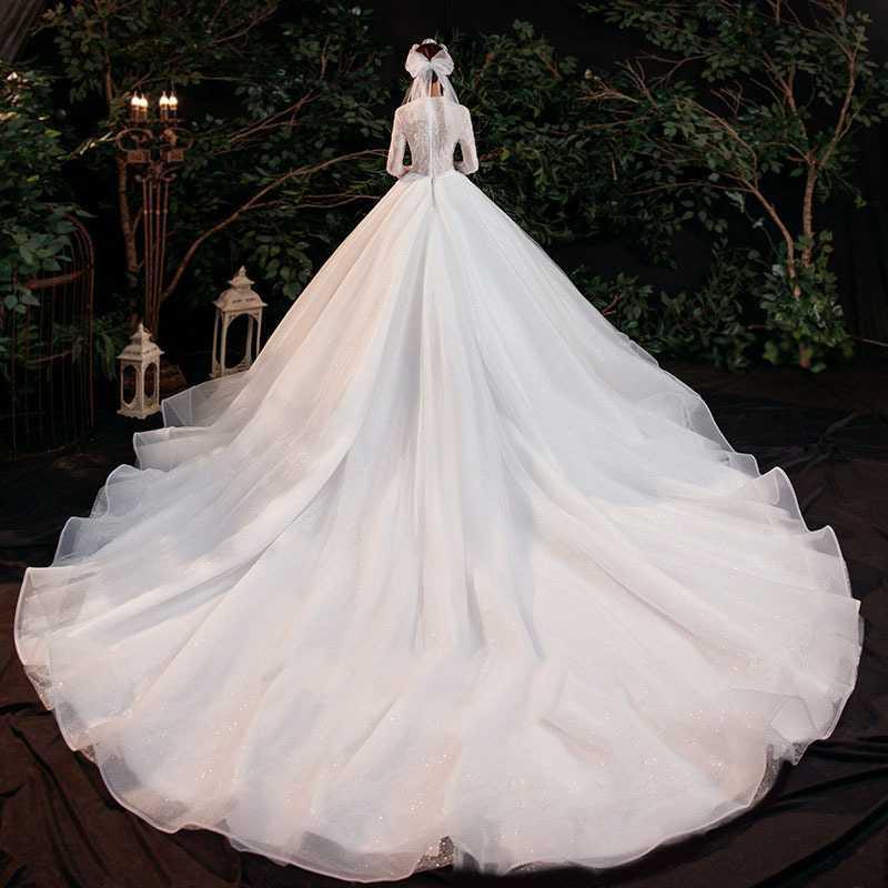 a flowing white wedding gown featuring a fitted bodice, temperament trailing long sleeves, and an expansive tulle skirt adorned with subtle glitter embodying elegant lace bridal temperament trailing style