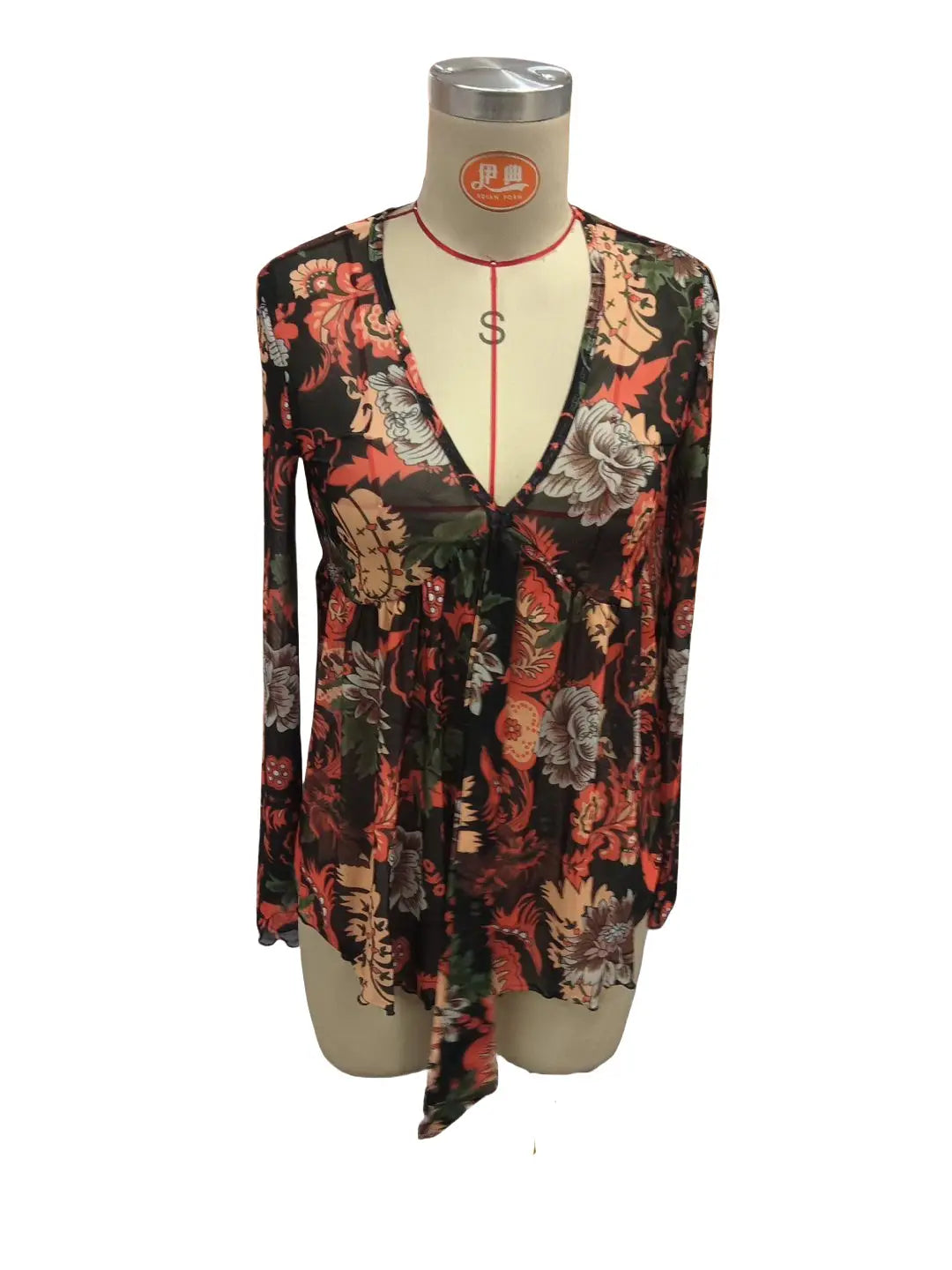 A long-sleeved v-neck mesh printed romper in dark fabric with an intricate floral pattern featuring reds oranges and muted greens and knotted flare sleeves.